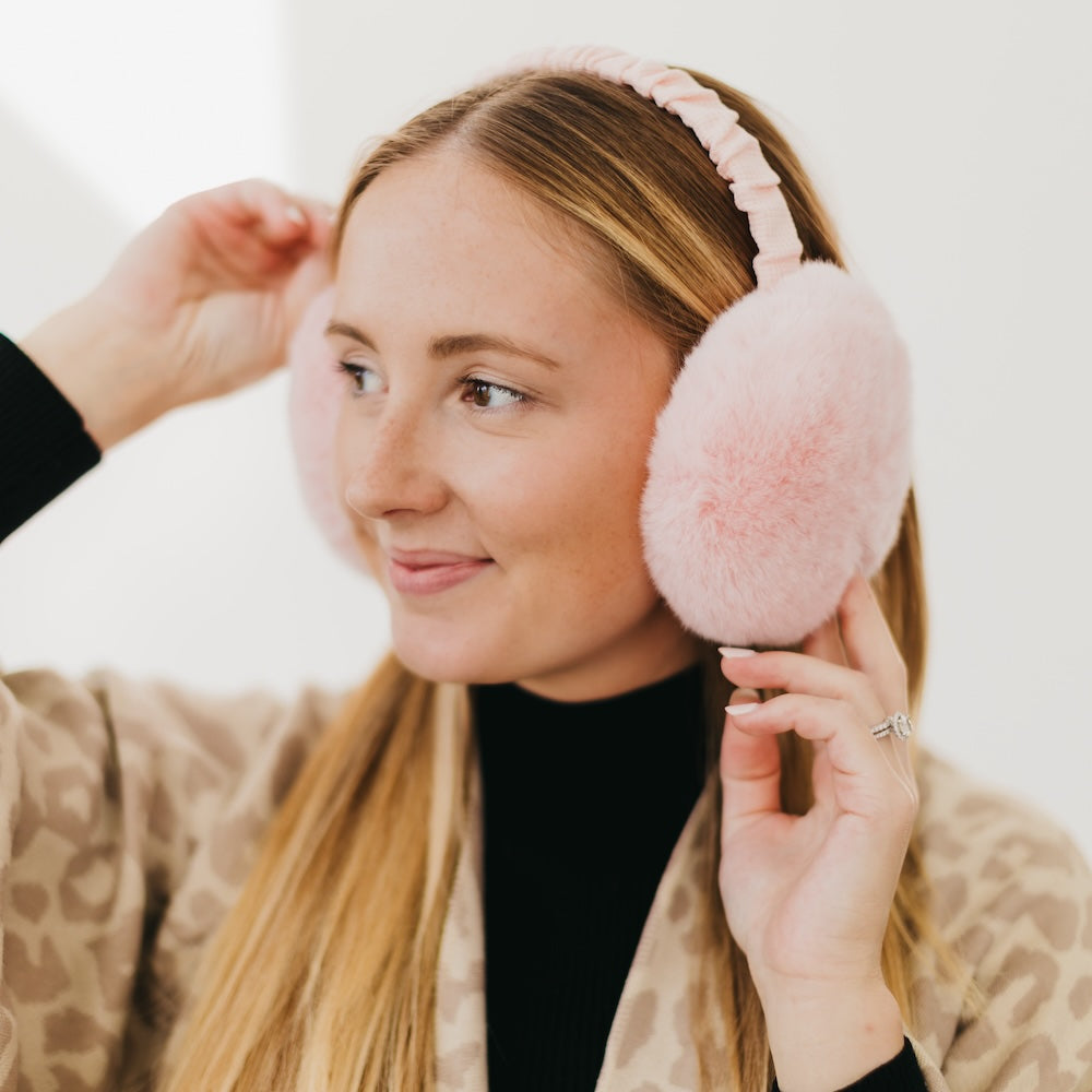 Woman wearing pink fluffy earmuffs against a white background