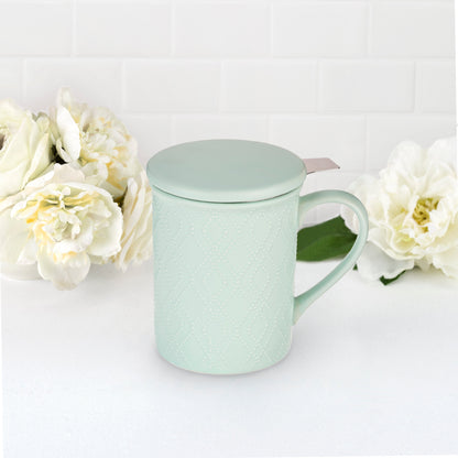 Mint green mug with tea infuser and lid on a white background with white flowers