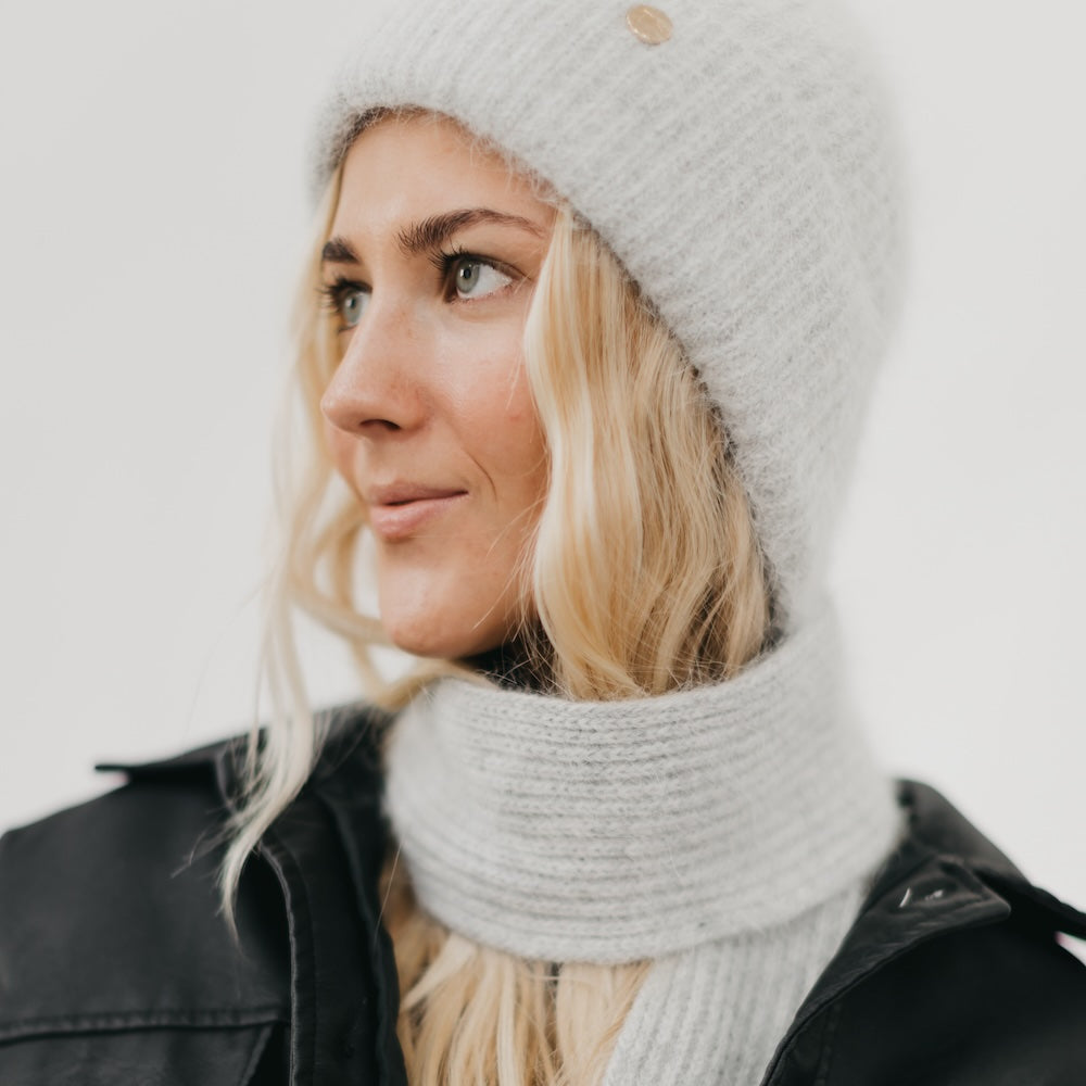 Woman wearing a gray knit beanie and scarf against a white background