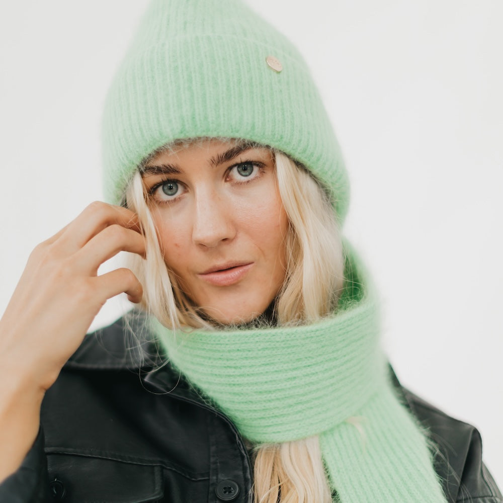 Person wearing a green knit hat and scarf against a white background