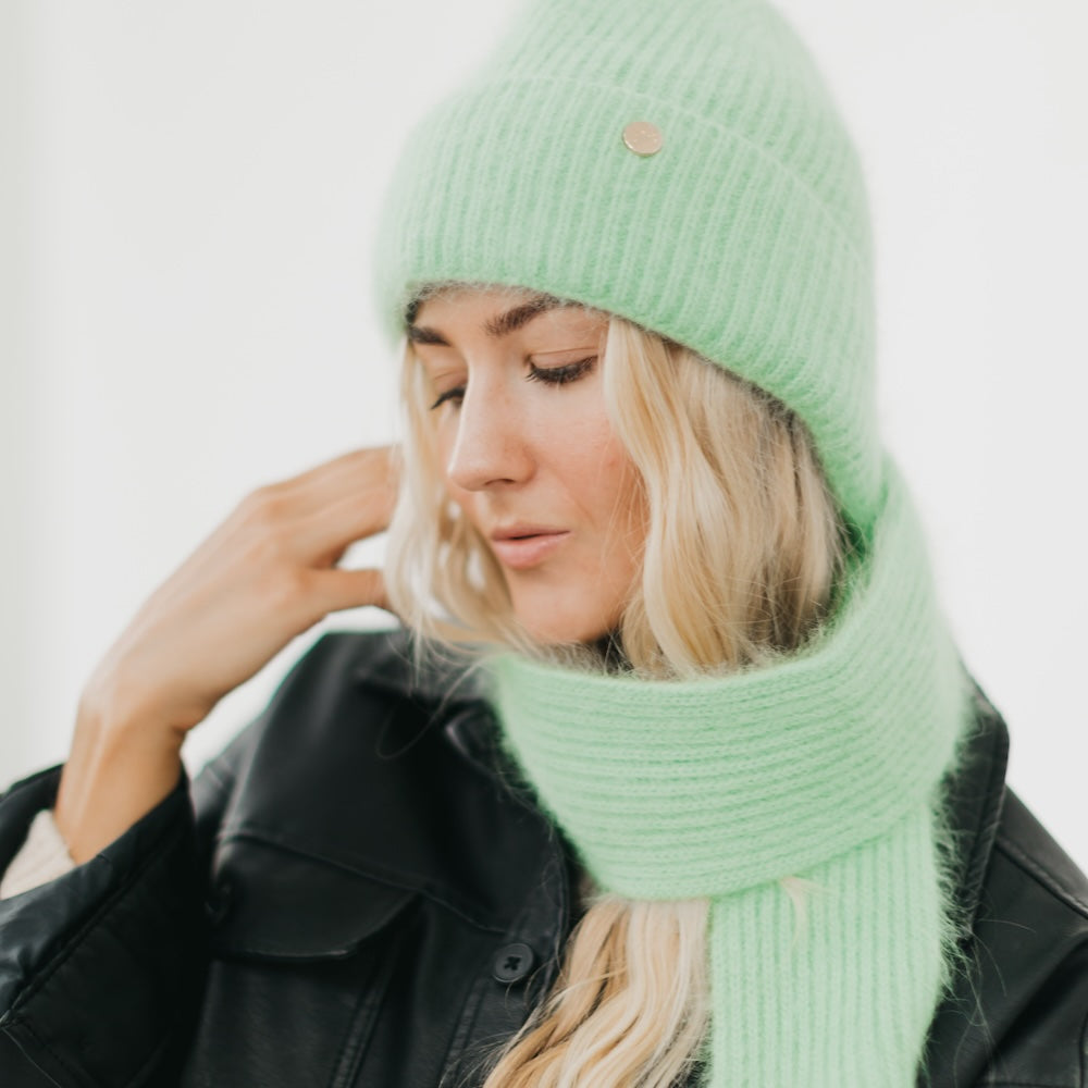 Woman wearing a green knit hat and scarf against a white background
