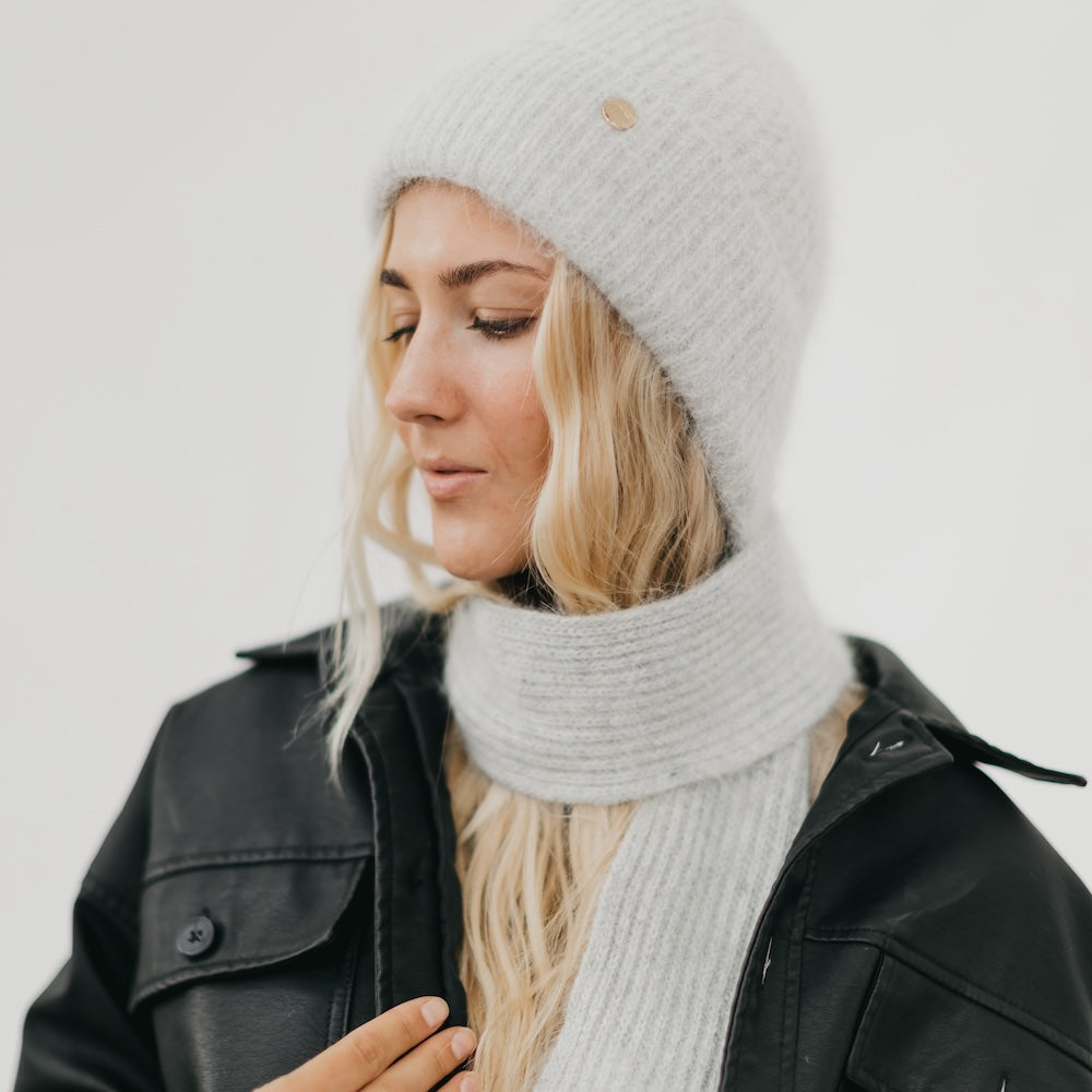 Woman wearing a white knit beanie and scarf against a light background