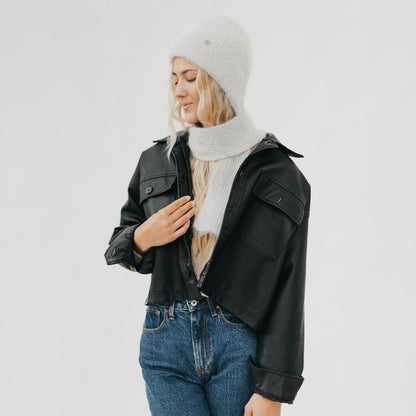 Person wearing a black jacket, white beanie, and scarf on a plain background