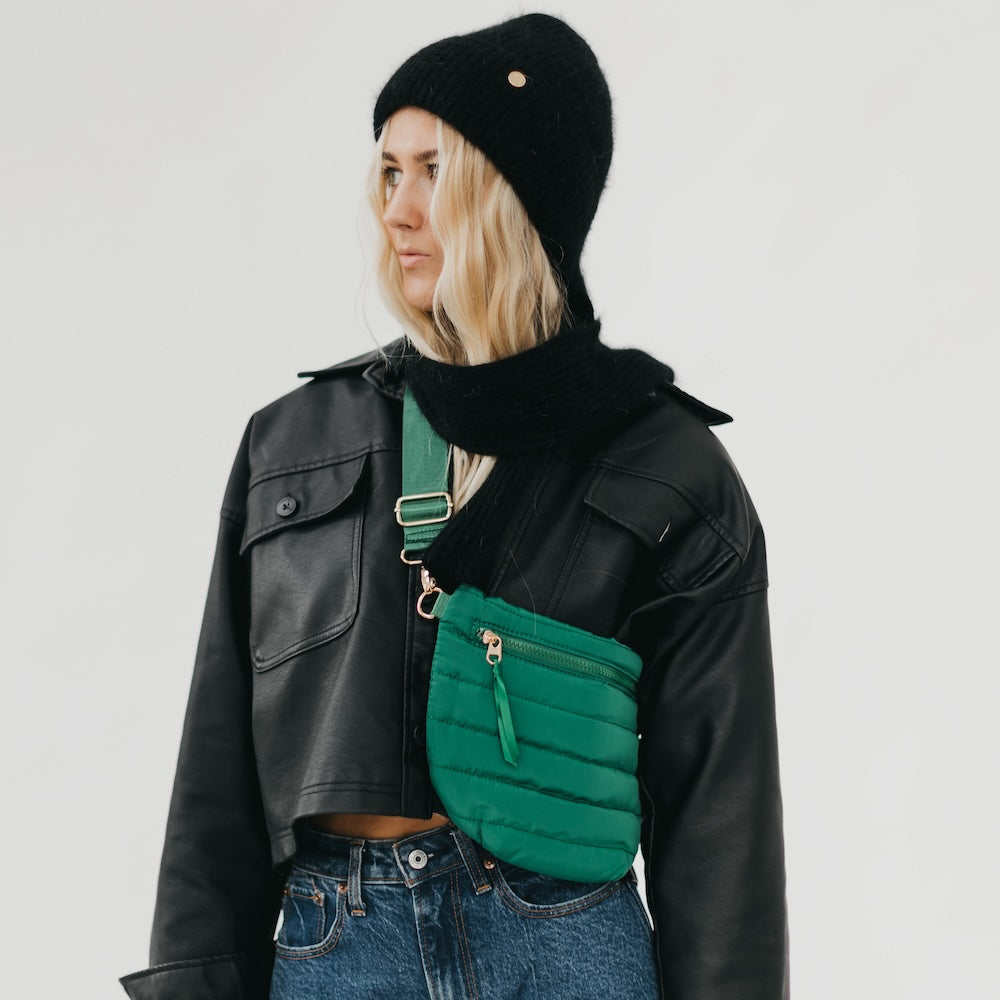 Person wearing a black leather jacket, black beanie, and green puffer bag on a plain background