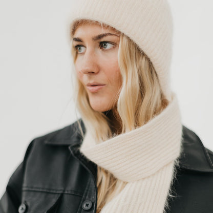 Person wearing a beige knit hat and scarf against a light background