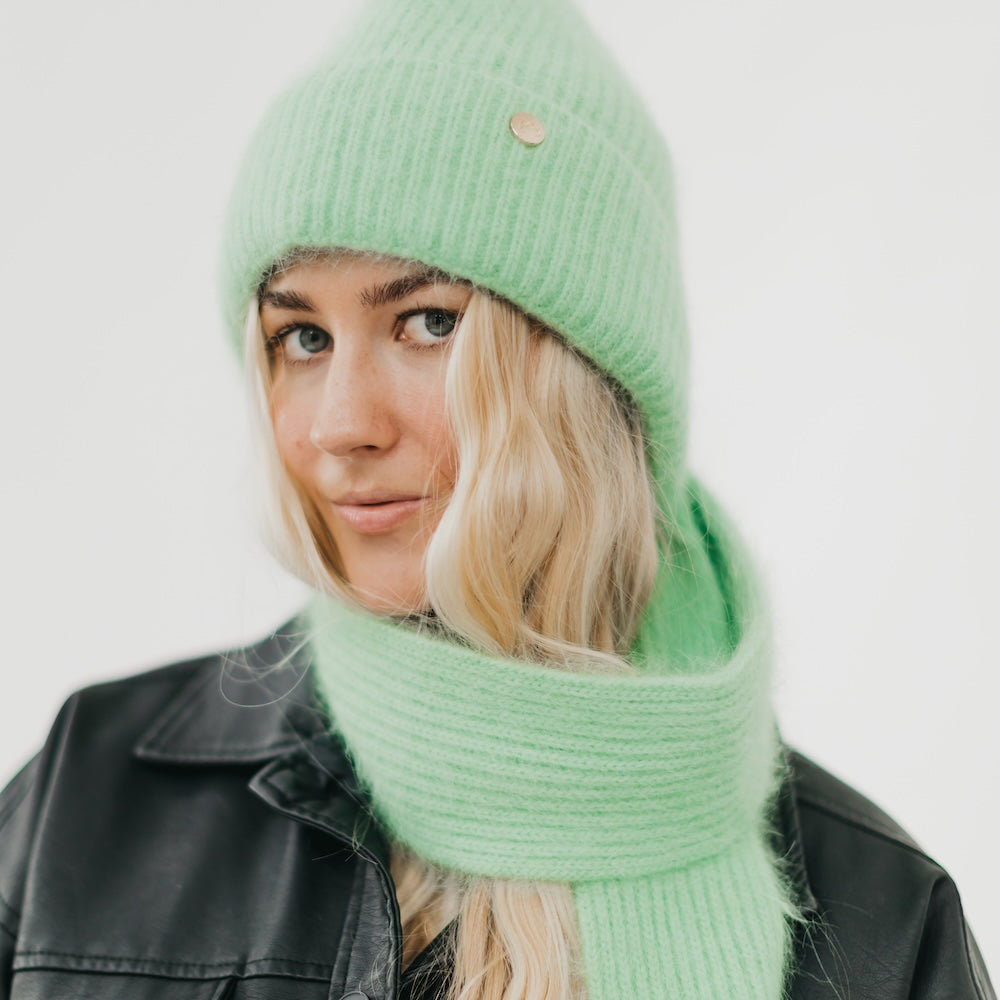 Person wearing a green knit hat and scarf against a white background