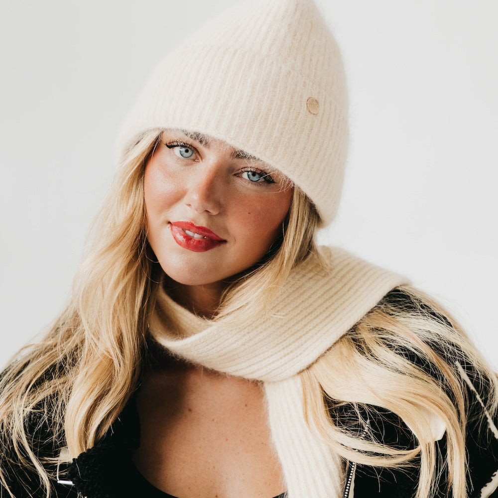 Woman wearing a beige knit beanie and scarf against a white background
