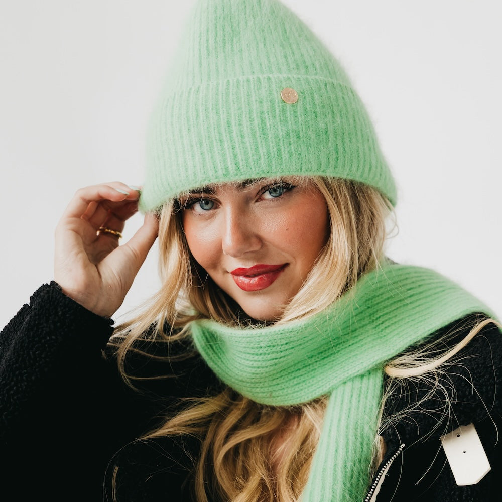 Woman wearing a green knit hat and scarf against a white background
