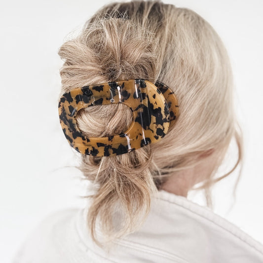 Person with a leopard print hair clip holding their hair back on a white background