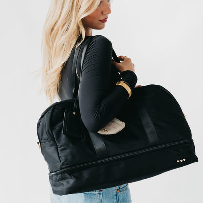 Woman holding a black duffel weekender bag against a plain background
