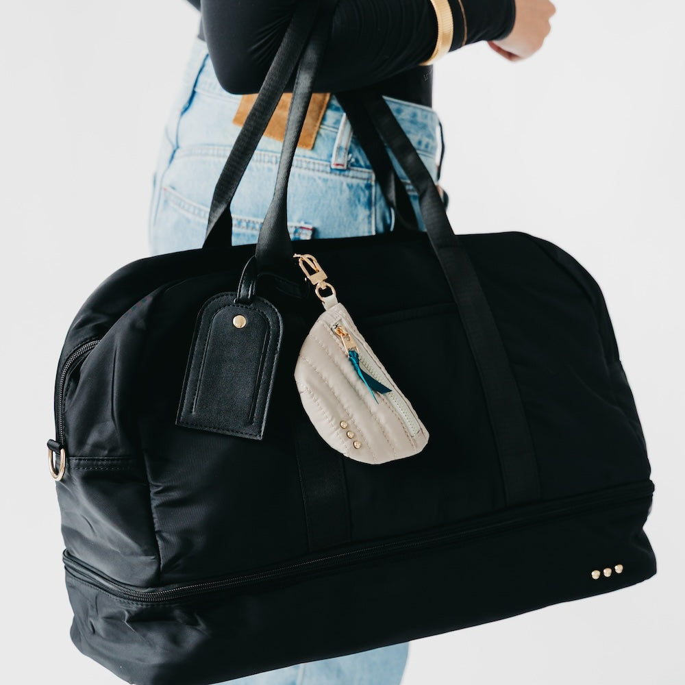 Black duffel bag weekender bag with a decorative tag held by a person against a light background