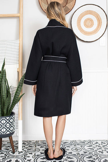 Person wearing a black Waffle Kimono Knee-Length robe with white trim in a room with decorative elements.