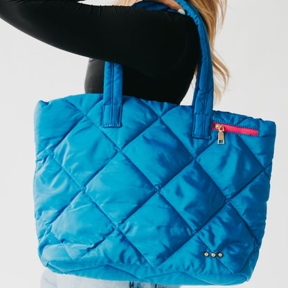 Blue quilted tote bag with a red zipper held by a person on a light gray background