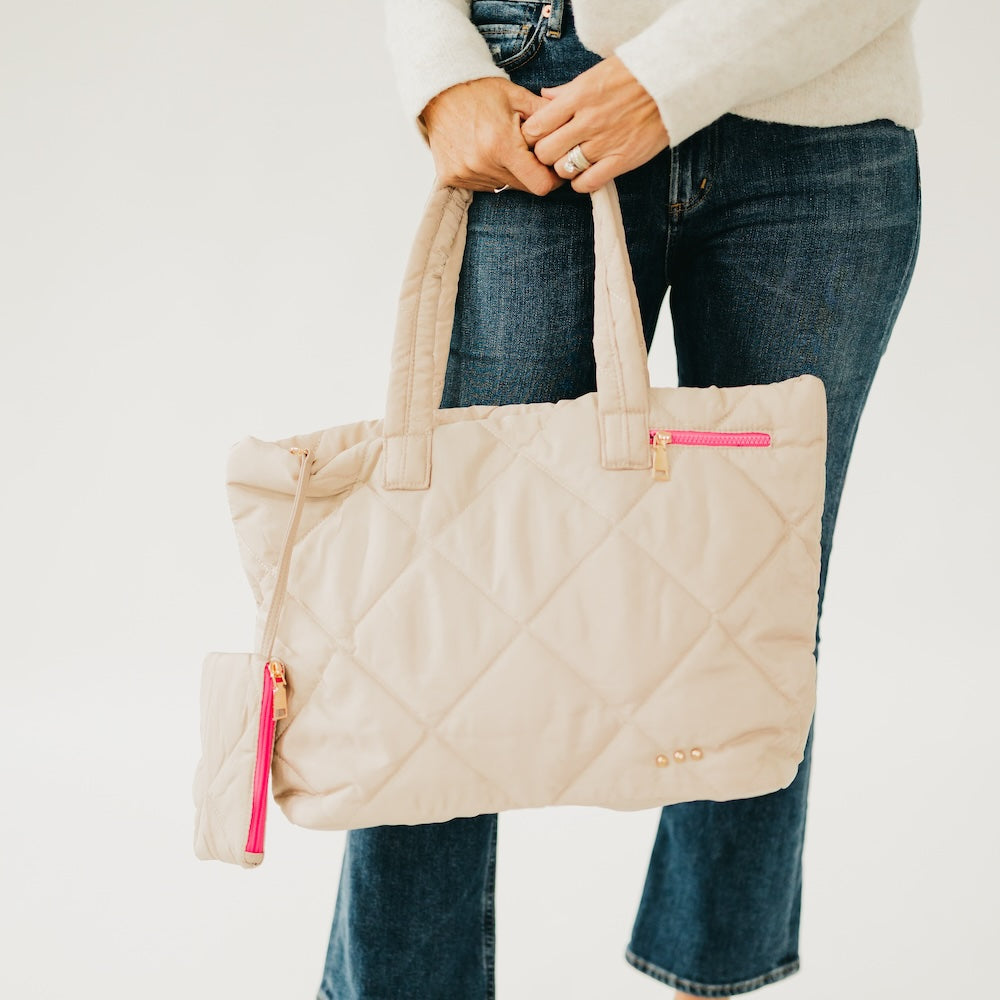 Person holding a beige quilted handbag with pink zipper on a white background