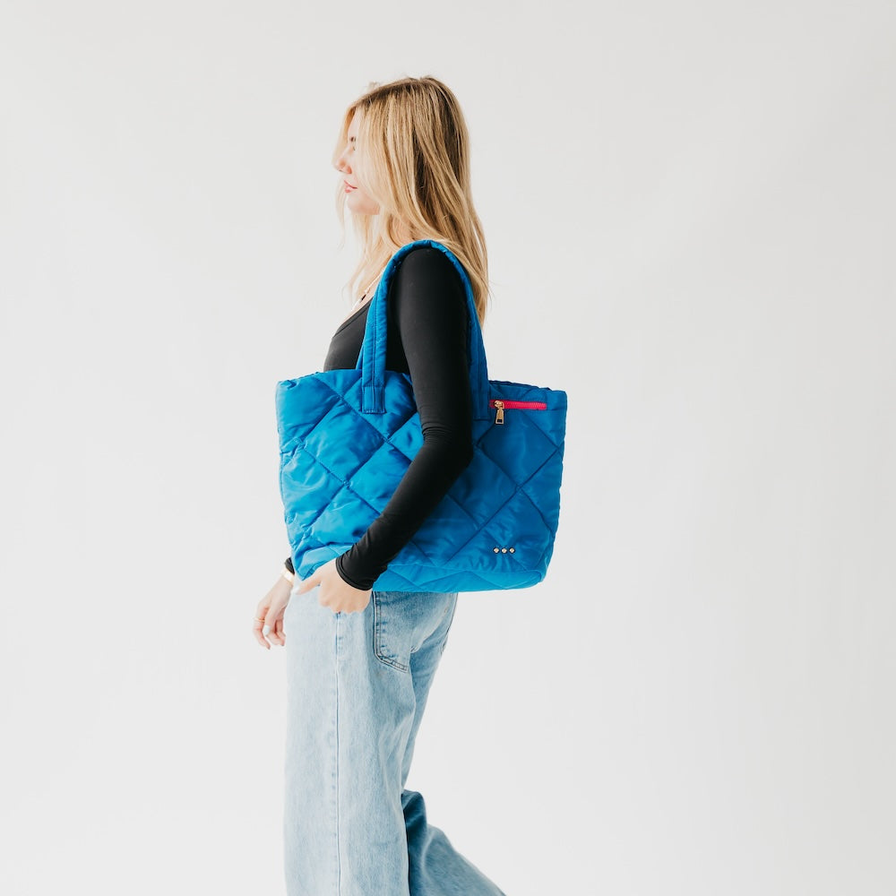 Woman holding a blue quilted tote bag against a white background