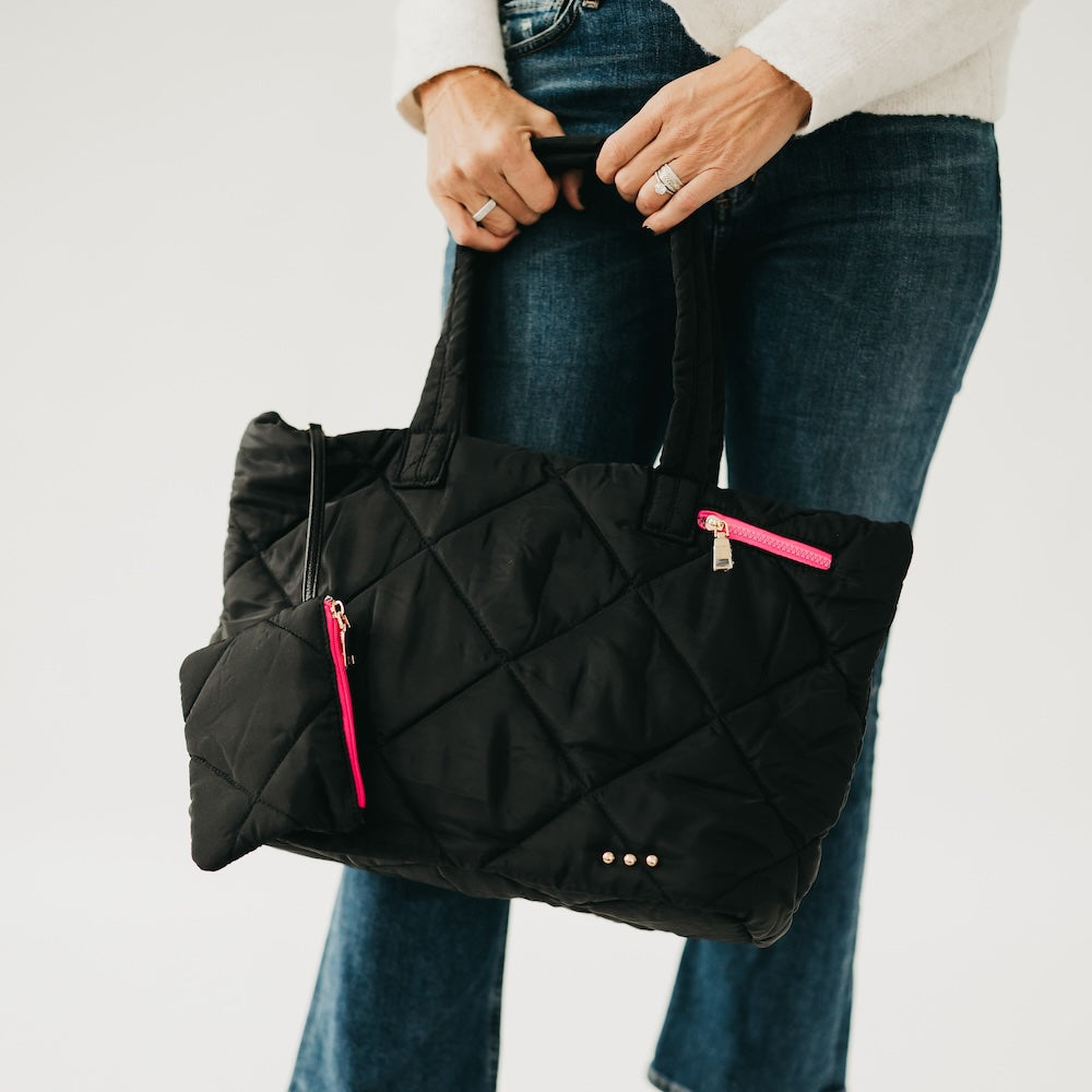 Person holding a black quilted bag with pink zippers against a white background