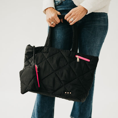 Person holding a black quilted bag with pink zippers against a white background