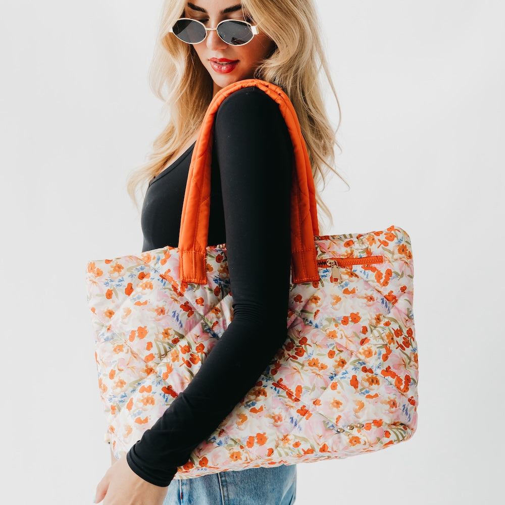 Woman holding a floral tote bag with an orange handle against a white background