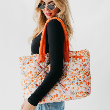 Woman holding a floral tote bag with an orange handle against a white background