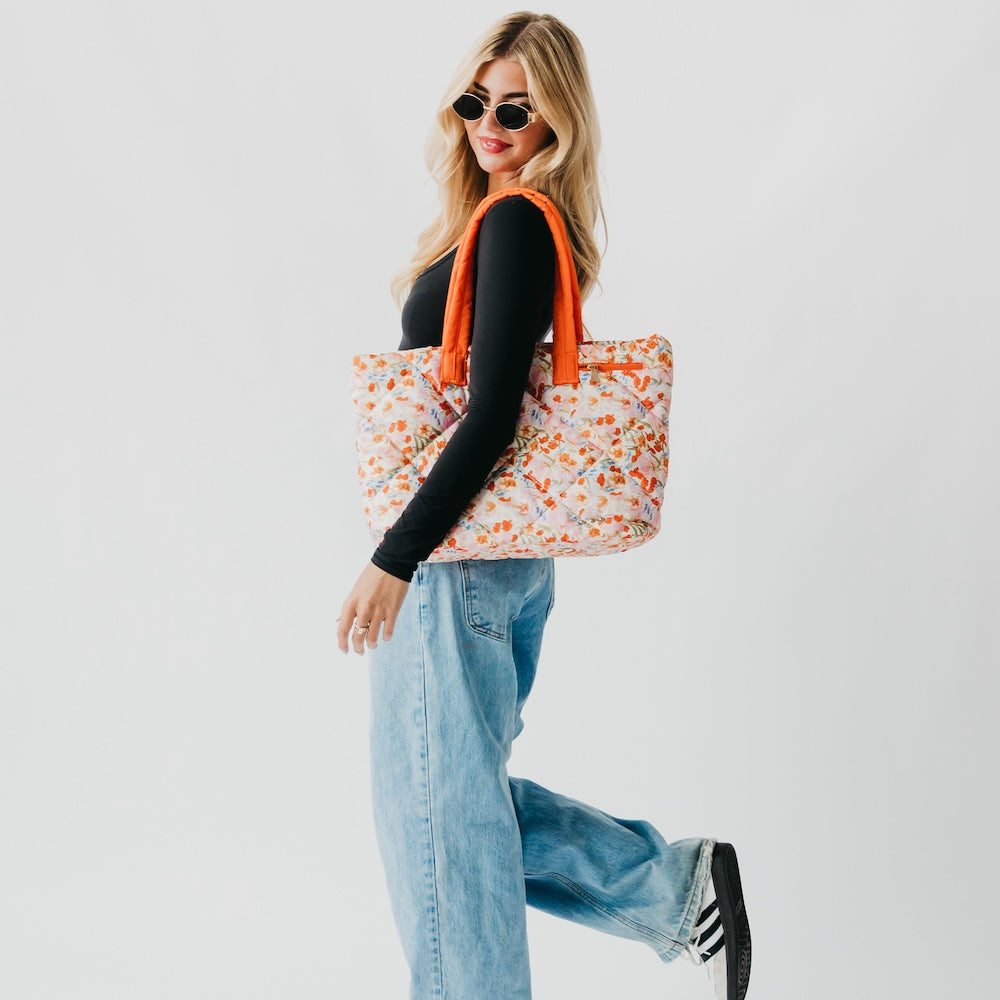 Woman holding a floral tote bag with an orange strap against a white background