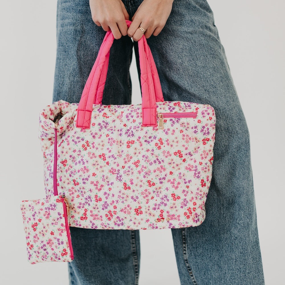 Floral tote bag with pink handles held by a person wearing jeans on a light gray background
