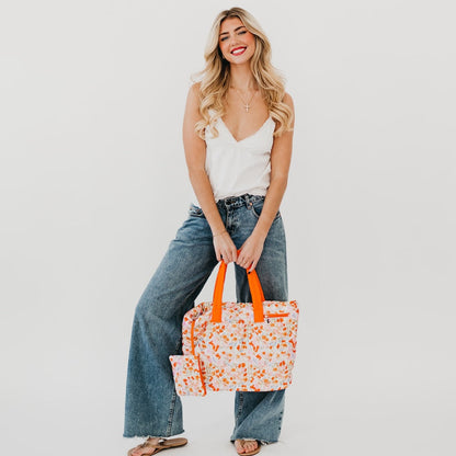 Woman holding a floral tote bag with orange handles against a plain background