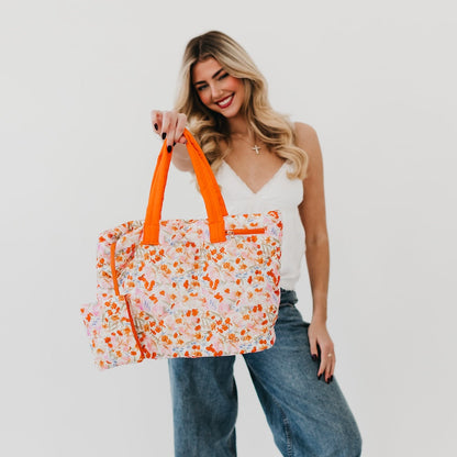 Woman holding a floral tote bag with orange handles against a white background