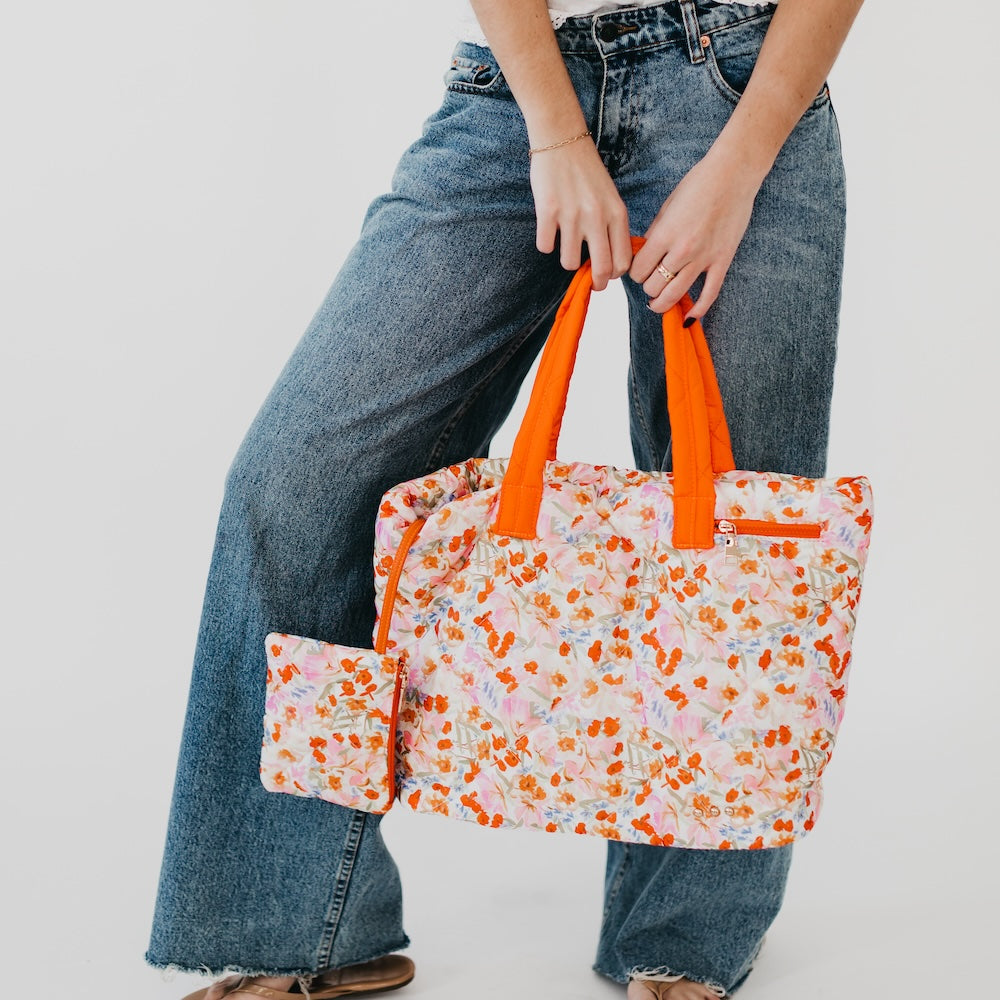 Person holding a floral tote bag with orange handles against a plain background