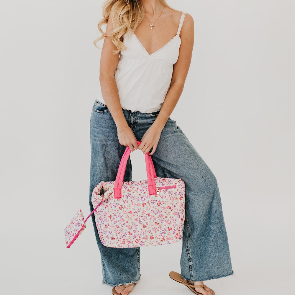 Woman holding a floral bag with pink handles against a plain background
