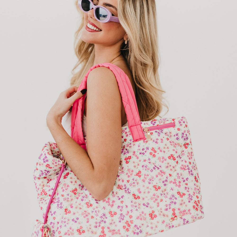 Woman holding a floral tote bag with pink accents against a white background