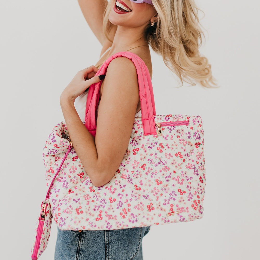 Woman holding a floral tote bag with pink straps against a plain background