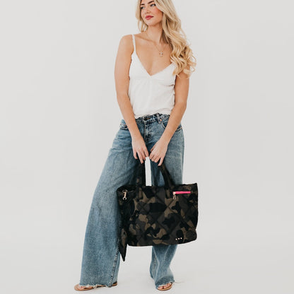 Woman holding a black and green patterned bag against a plain background
