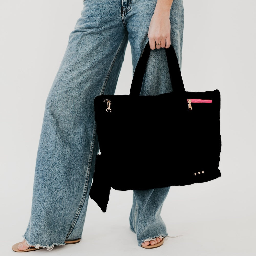 Person holding a black handbag with a pink zipper pocket against a plain background