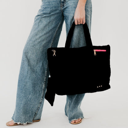 Person holding a black handbag with a pink zipper pocket against a plain background