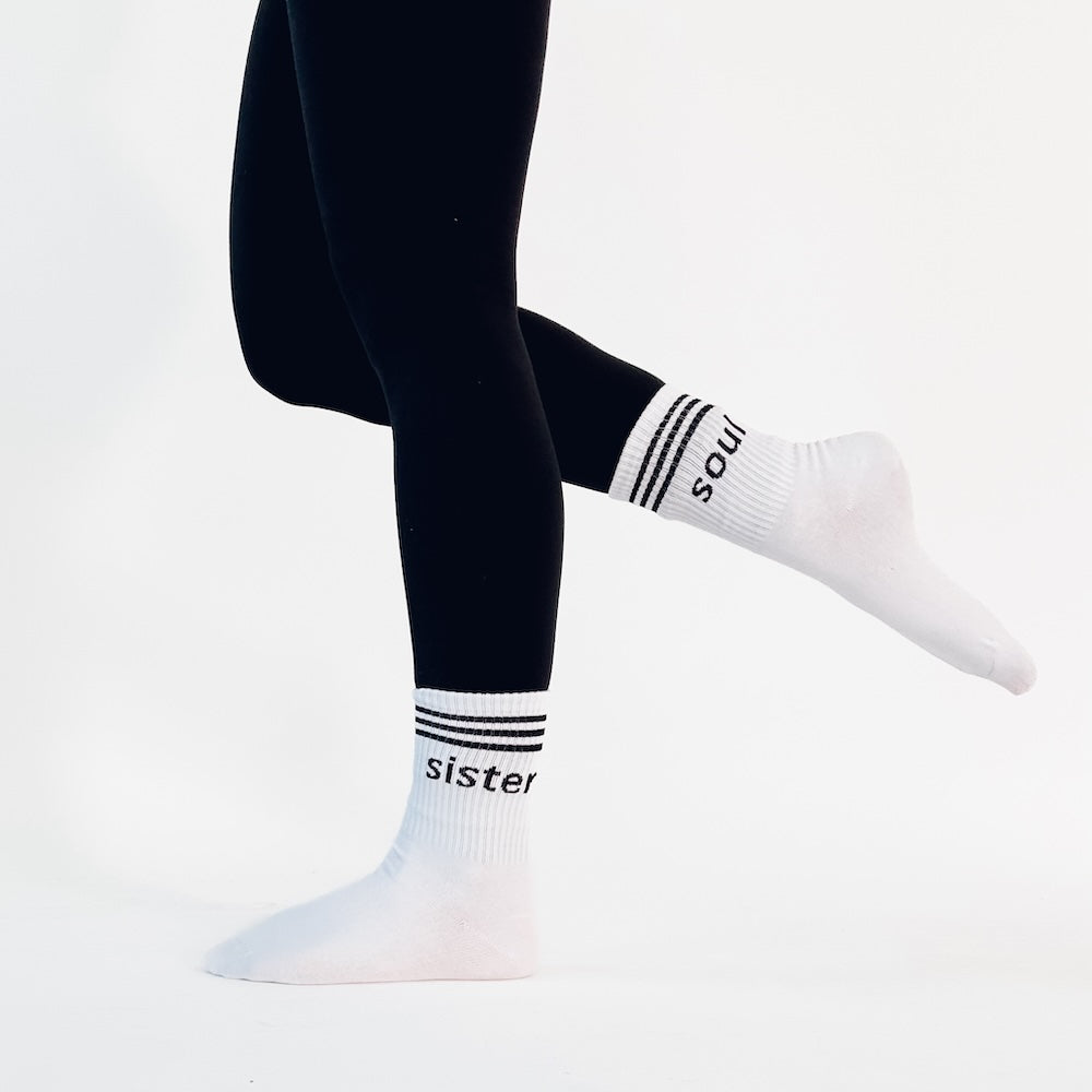 White socks with 'sister' and 'soul' text worn with black leggings on a white background