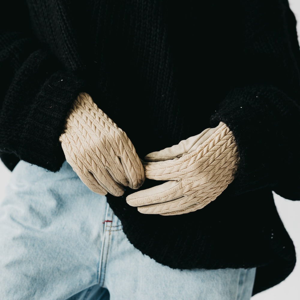 Close-up of beige gloves held together against a blurred snowy background