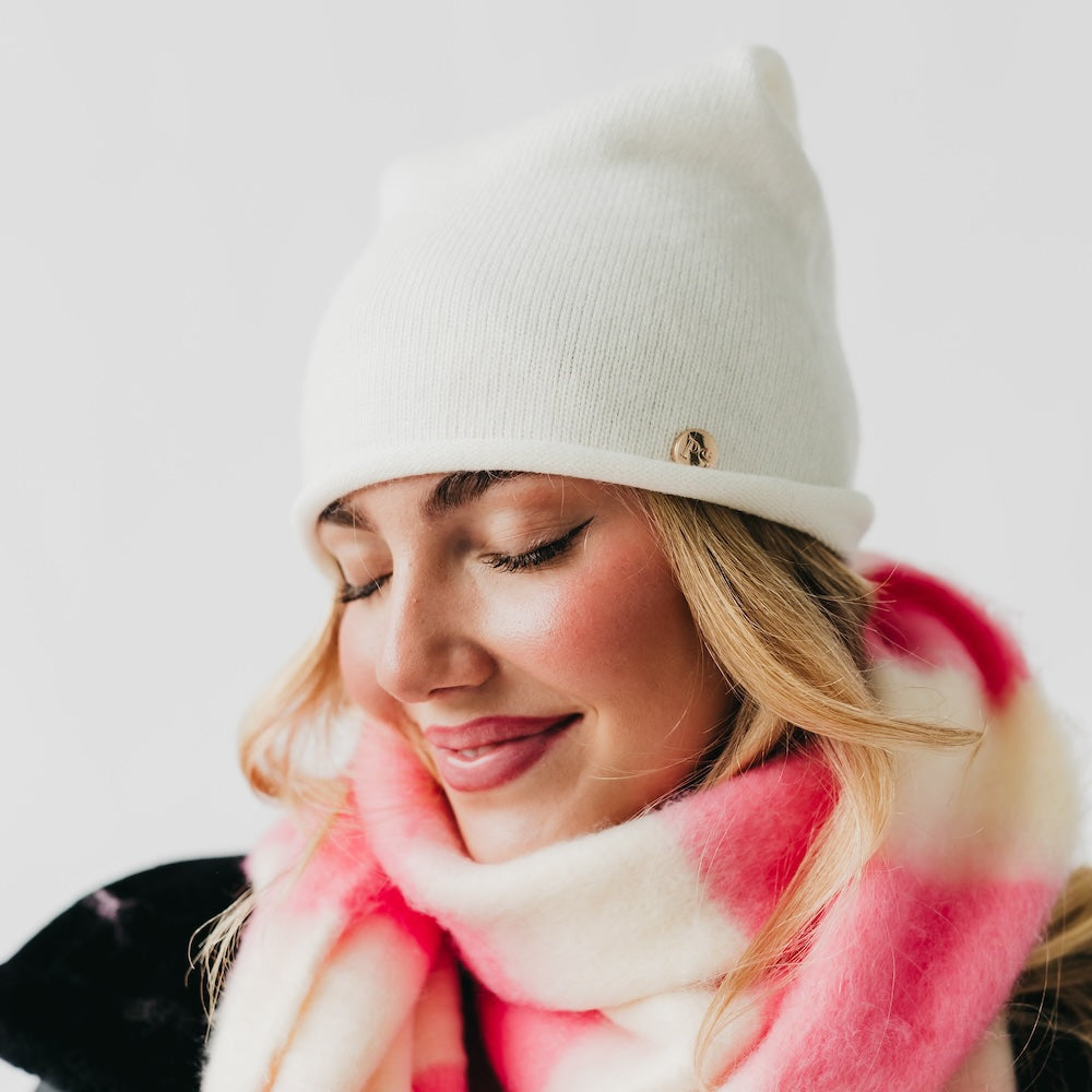 Woman wearing a white beanie and pink scarf against a light background