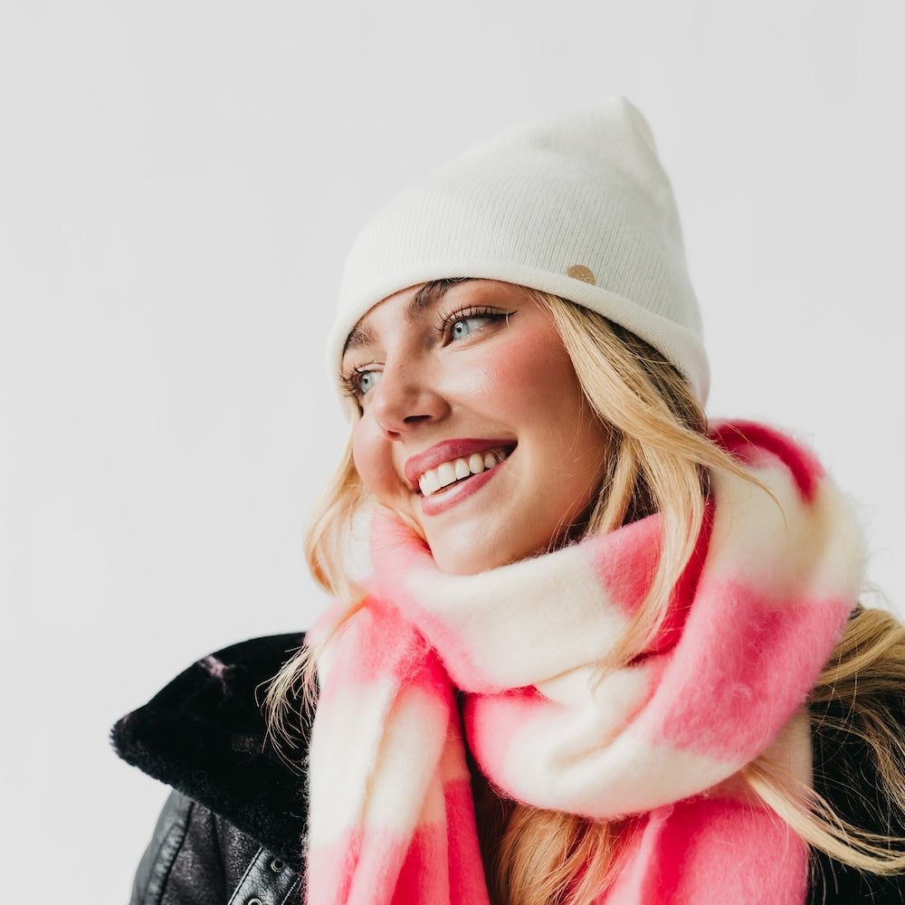 Woman wearing a white beanie and pink scarf against a light background