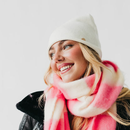 Woman wearing a white beanie and pink scarf against a light background