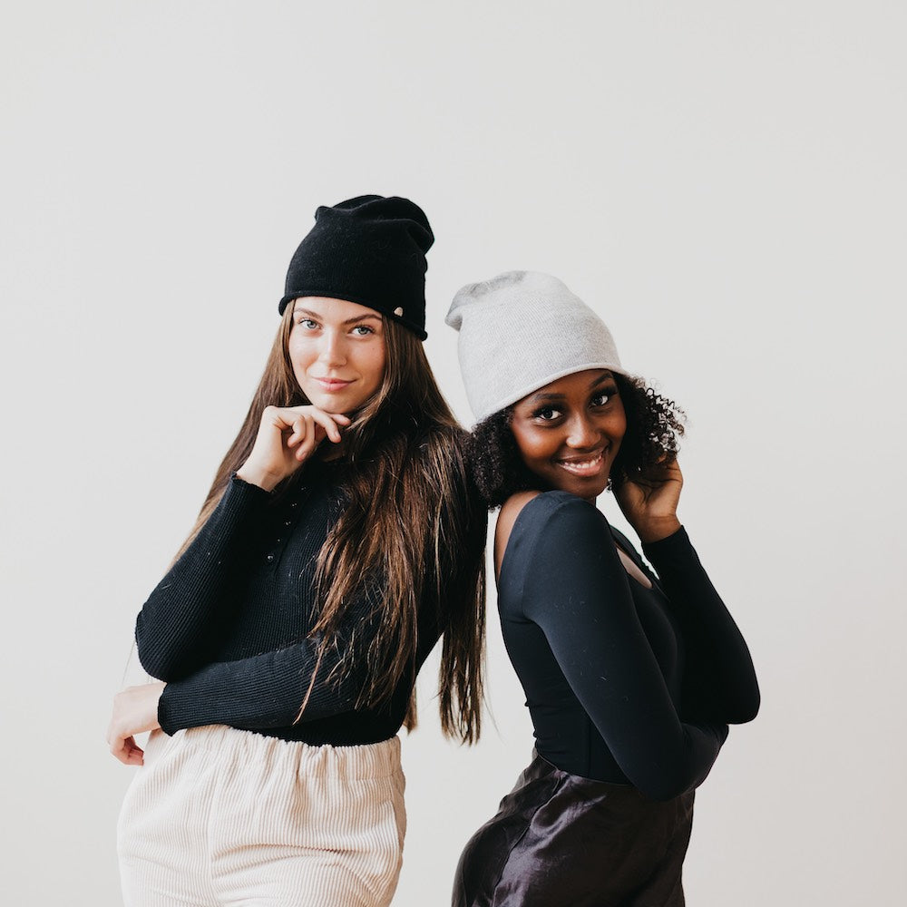 Two women wearing black and white beanies against a plain background