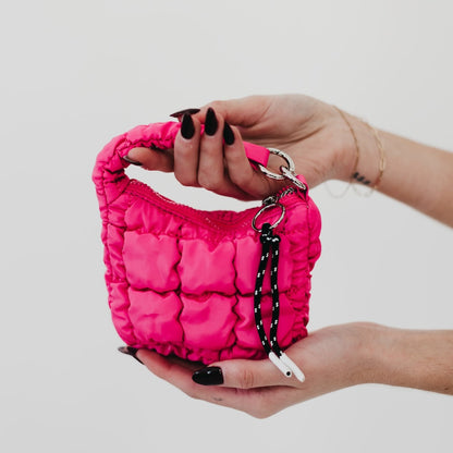 Person holding a small pink quilted handbag with a keychain on a light gray background