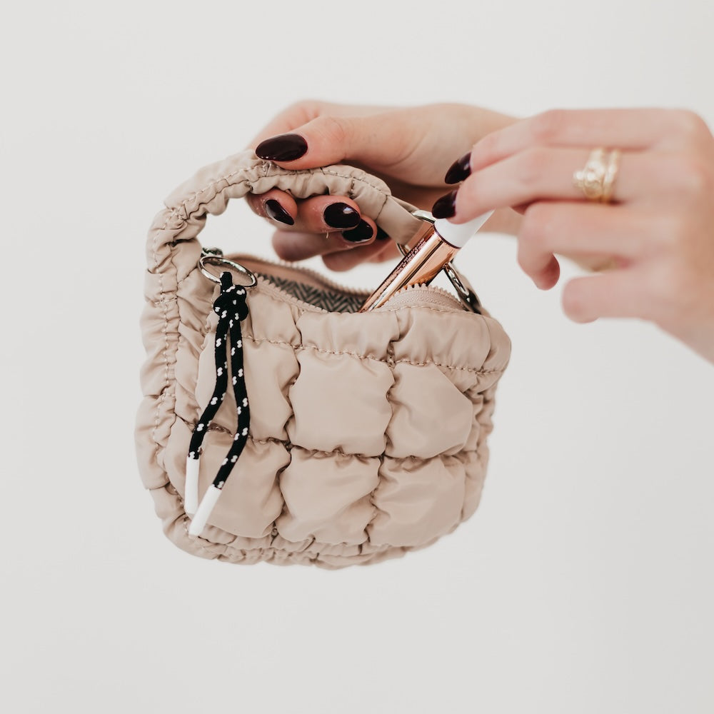 Hand holding a beige textured pouch with a mirror and black strap on a light background