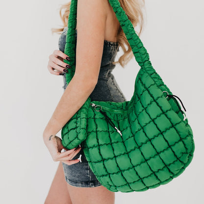 Green quilted handbag held by a person on a plain background