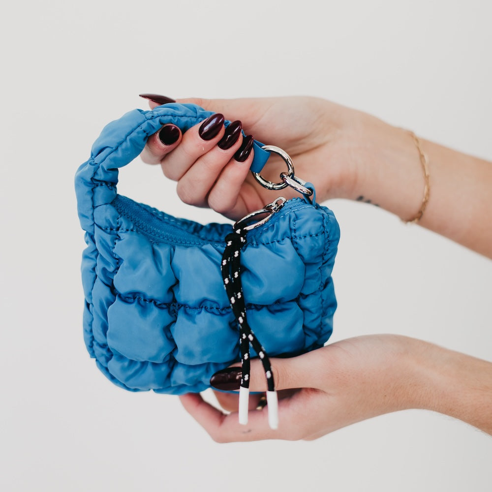 Blue textured bag held by a hand with dark nail polish on a light background