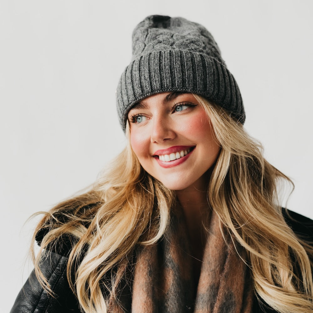 Woman wearing a gray knit beanie with satin lined interior and scarf against a white background