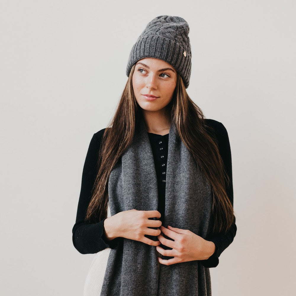 Woman wearing a gray knit beanie with satin lined interior and scarf against a plain background