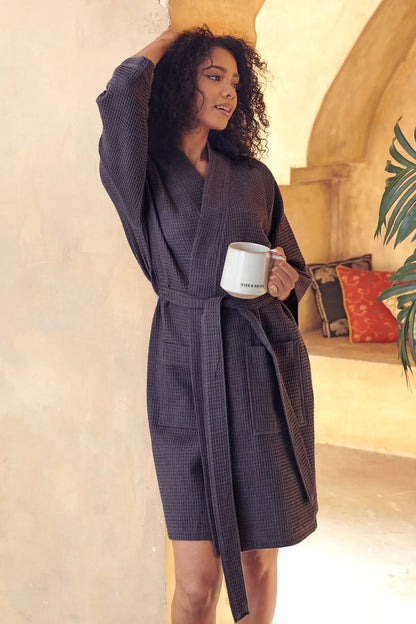 Woman in a dark gray Waffle Kimono Knee-Length robe holding a mug in a warm, indoor setting.