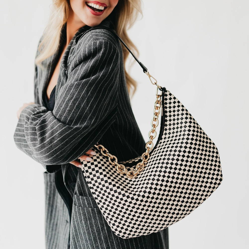 Woman holding a black and white checkered handbag with a gold chain strap.