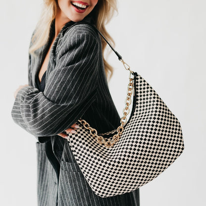 Woman holding a black and white checkered handbag with a gold chain strap.
