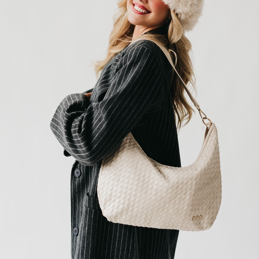 Woman holding a beige textured handbag against a plain background